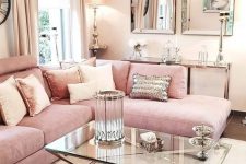 a glam and shiny feminine living room with a pink sofa, a glass coffee table, mirrors, a crystal chandelier and pink and shiny pillows