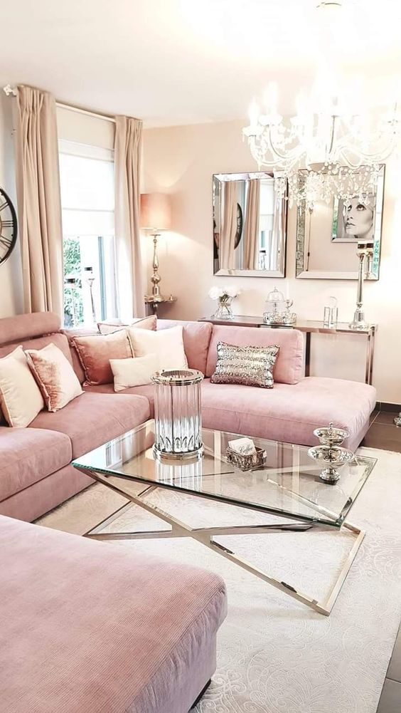 a glam and shiny feminine living room with a pink sofa, a glass coffee table, mirrors, a crystal chandelier and pink and shiny pillows
