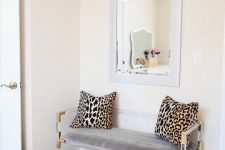 a glam entryway with an acrylic bench with leopard print pillows, a shiny gold pouf and simple layered rugs is stylish and lively