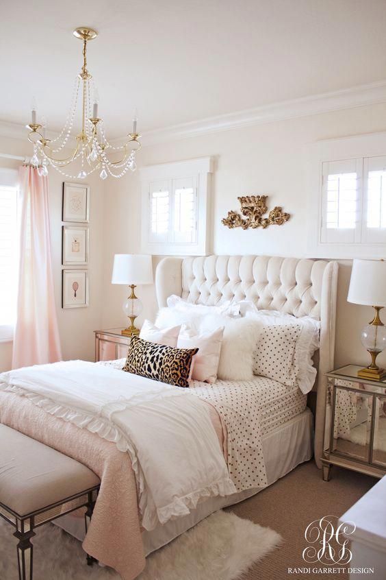 a glam girlish bedroom with an upholstered bed, mirrored nightstands and a bench, a crystal chandelier and touches of light pink