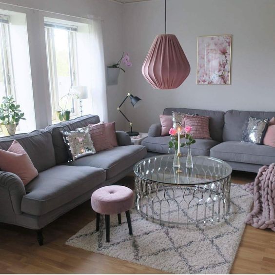 a lovely feminine living room with grey sofas, pink pillows, a stool and a pendant lamp, a chic and shiny coffee table and a floral print