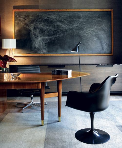 a luxurious home office with an oval wooden desk, black leather chairs and an oversized dark artwork