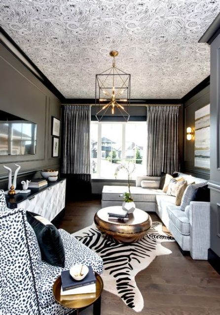 a luxurious living room with dark walls, a white sectional with colorful pillows, a chic chandelier, a zebra print rug and a Dolmatin print chair