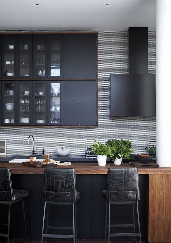 a masculine kitchen with graphite grey cabinets, a wooden kitchen island, black leather stools and a black hood