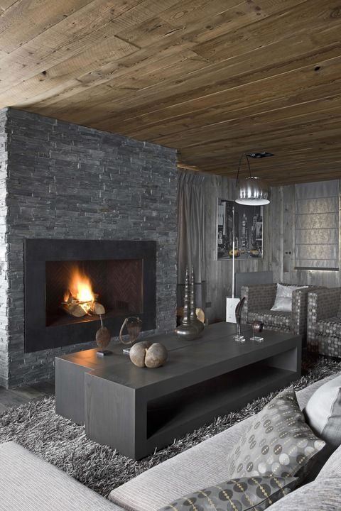 a masculine living room with a stone clad fireplace, wooden tables, a faux fur rug, upholstered furniture and lamps
