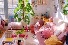 a maximalist girlish living room with light pink walls, a pink sofa with pink and yellow pillows, a low coffee table and some greenery