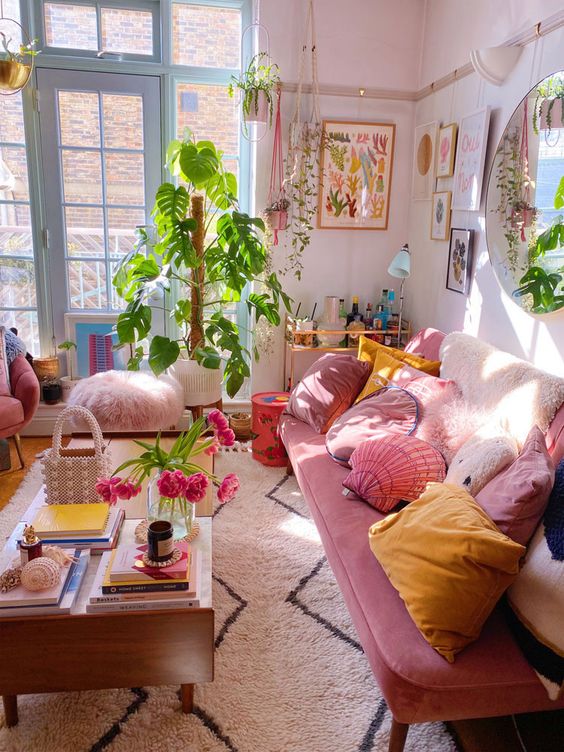 a maximalist girlish living room with light pink walls, a pink sofa with pink and yellow pillows, a low coffee table and some greenery