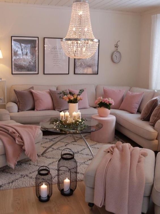 a modern girlish space with neutral walls, a neutral corner sofa and matching chairs, mauve and pink pillows and blankets and candle lanterns plus a gorgeous chandelier