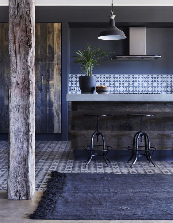 a navy kitchen with blue walls, a rug, printed tiles, a rough kitchen island with a stone countertop looks chic