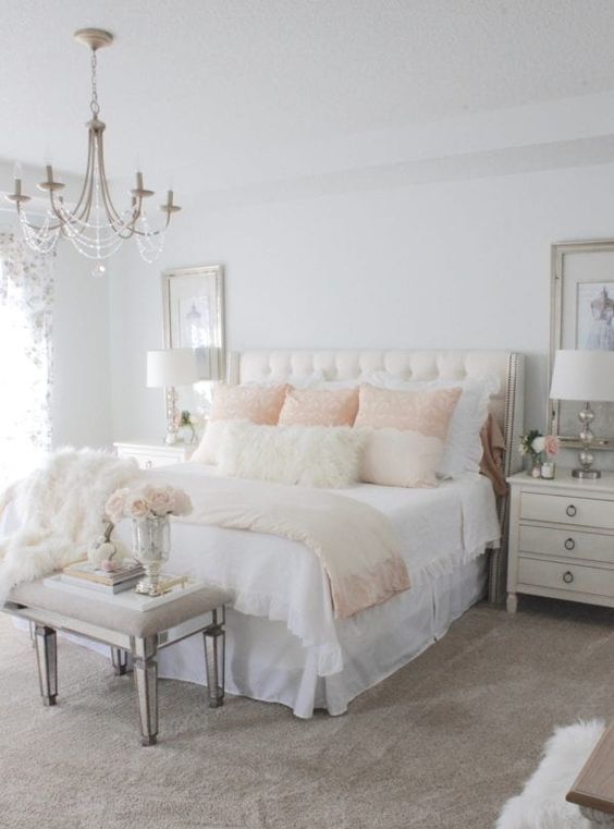 a neutral vintage bedroom with elegant furniture, neutral and pastel textiles, a crystal chandelier and large artworks plus mirror touches