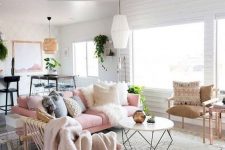 a pretty Scandi living room with a feminine feel, a pink sofa with lots of pillows, a table with a geo base, a woven chair and other chairs, potted greenery