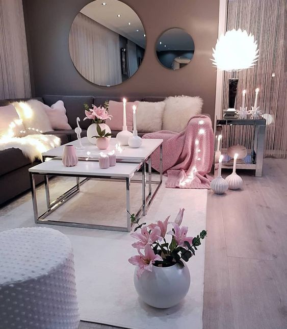 a pretty and chic living room with a grey corner sofa, a duo of coffee tables, a polka dot pouf, round mirrors, pink accessories and blooms