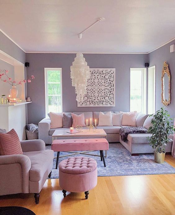 a pretty living room with lilac walls, a lilac sofa, a pink chair and a pouf, a pink bench, a catchy chandelier and a mirror in an ornated frame