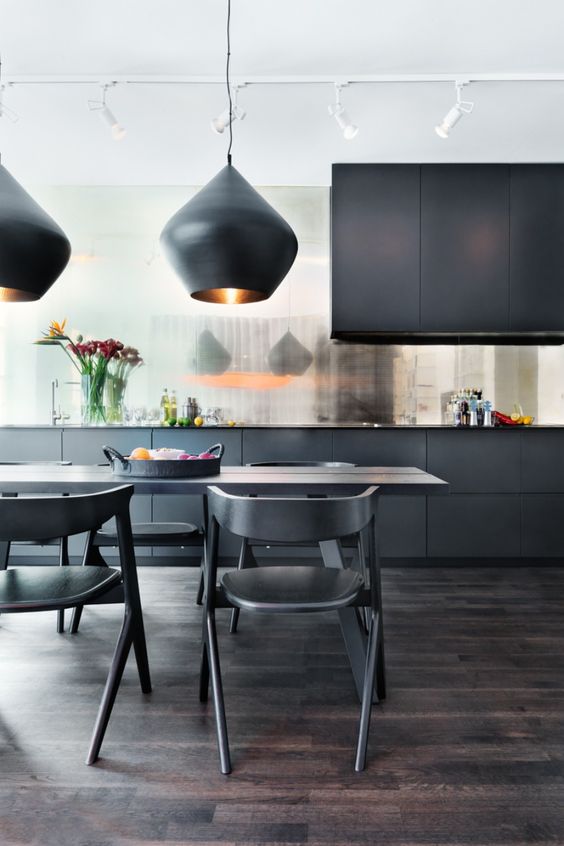 a refined and elegant black kitchen with a shiny backsplash, sleek cabinets, a dining set in black and catchy pendant lamps