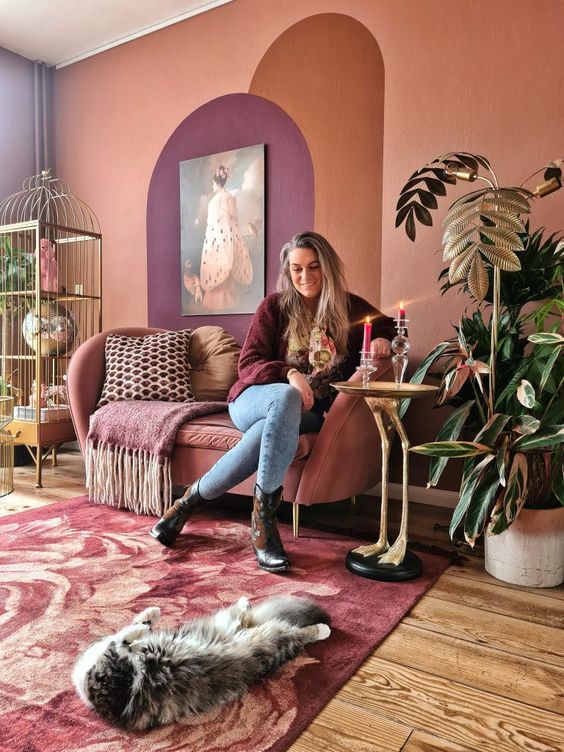 a refined eclectic living room with a rust accent wall, a mauve sofa, a burgundy and pink rug, potted plants and a cage as a storage unit