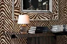 a refined entryway with a brown and white zebra print wall, a dark wooden console table, stacks of books, a table lamp and an artwork in a zebra printed frame