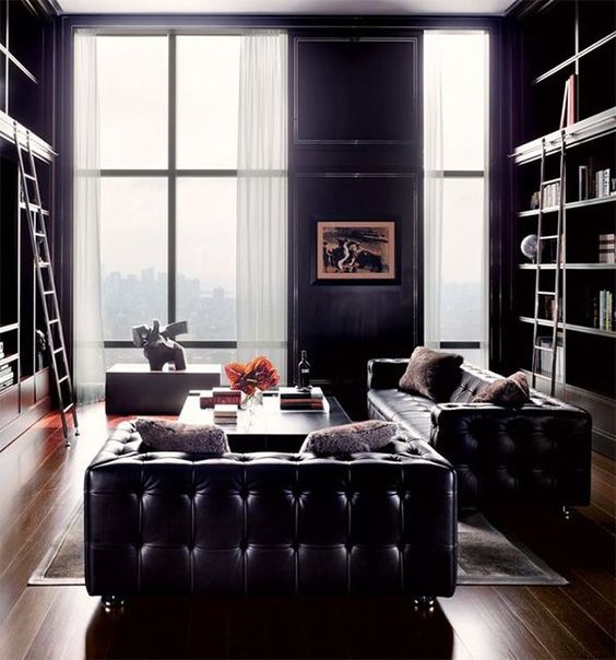 a refined living room with black leather furniture, large book shelf units, neutral curtains and some coffee tables