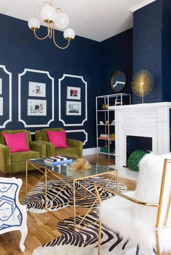 a refined living room with navy walls, a faux fireplace, green chairs with hot pillows, zebra print rugs, a glass coffee table and chairs