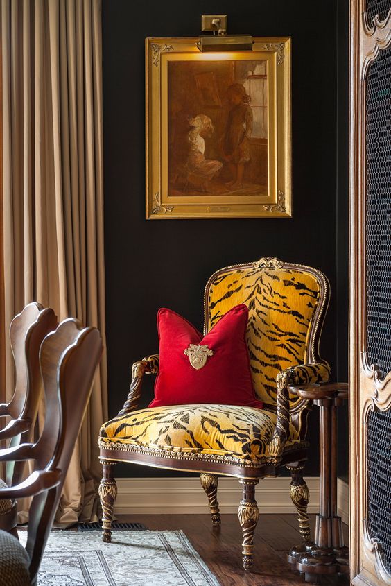 a refined vintage space with black walls, a yellow and black zebra print chair with a red pillow, an artwork and a vintage wardrobe with cane