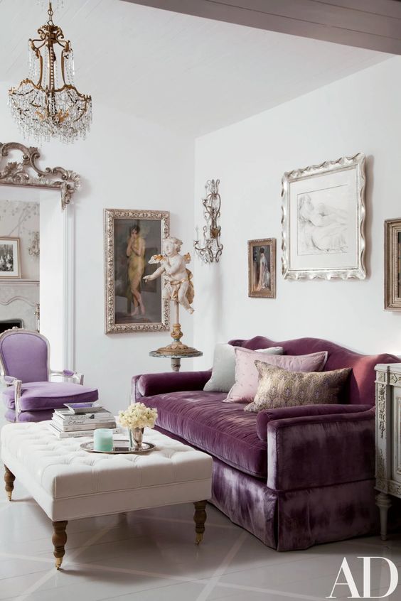 a sophisticated living room with a purple sofa and a lilac chair, a creamy ottoman, a crystal chandelier, beautiful and refined artworks