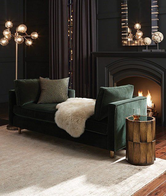 a sophisticated men's room with black walls and a fireplace, a mirror, some lamps, a side table and a green couch