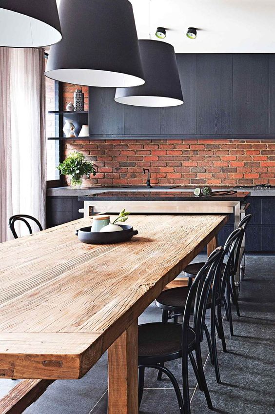 a stylish masculine kitchen with a red brick backsplash and black cabinets and pendant lamps