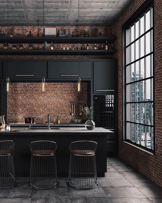 a stylish moody kitchen with black cabinets, gold touches, a large kitchen island and red brick walls