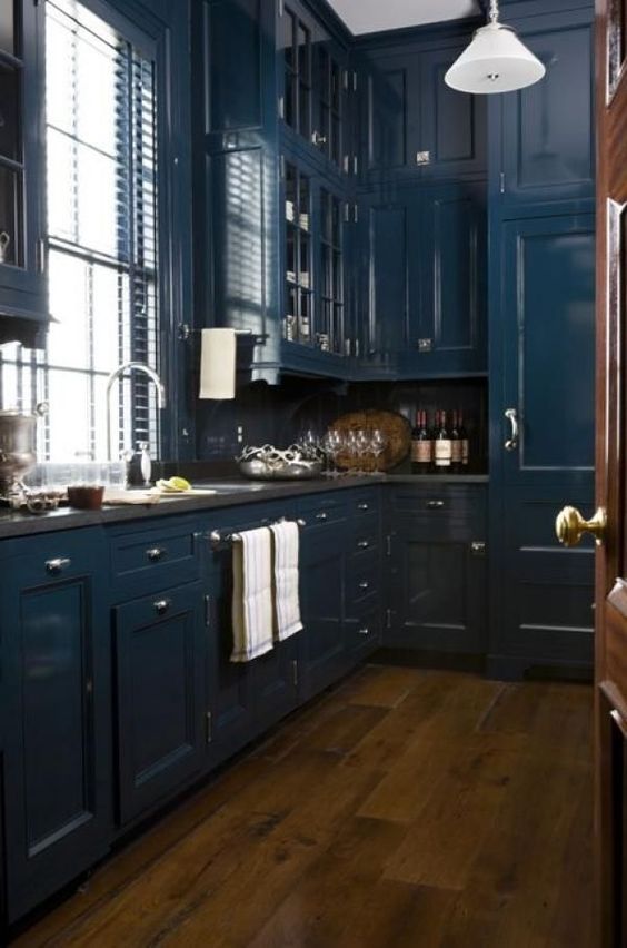 a teal and rich-stained kitchen with stone countertops, metallic handles and white pendant lamps