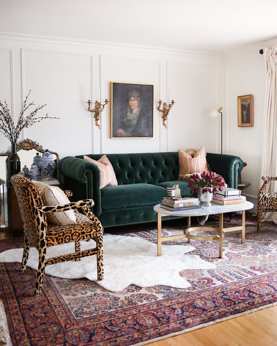 a vintage inspired living room with a dark green sofa, leopard print chairs, a coffee table and layered rugs plus cool and chic art