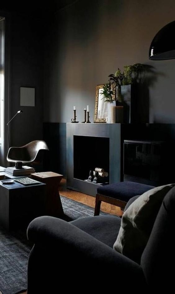 a welcoming dark manly room with black walls, a fireplace, some dark upholstered furniture, lamps and candles