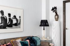 a whimsical living room with a leopard print sofa, a moody floral rug, a black coffee table, a print, a black chair and a vase with black callas