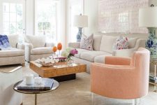 an eclectic and feminine living room with creamy seating furniture, a peachy chair on acrylic legs, a slab coffee table and a pink artwork plus floral pillows