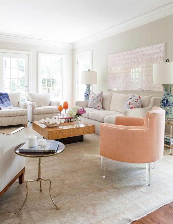 an eclectic and feminine living room with creamy seating furniture, a peachy chair on acrylic legs, a slab coffee table and a pink artwork plus floral pillows