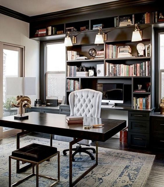 an elegant and chic masculine home office with a wooden desk and a stool, a built-in bookcase and much natural ligjt