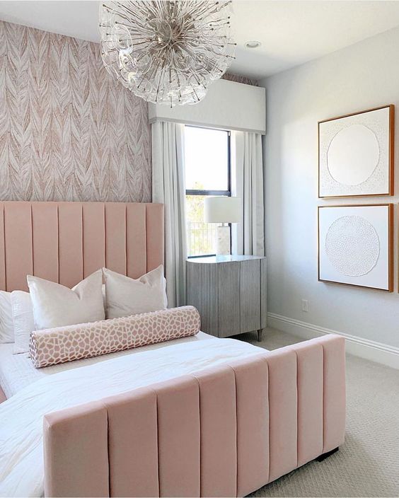 an elegant and laconic feminine bedroom with a wallpaper wall, a pink bed, a catchy chandelier and abstract artworks