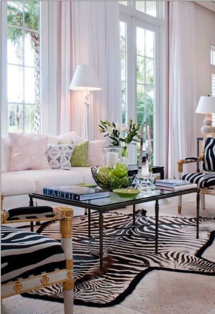 an elegant living room with a creamy sofa and pastel pillows, a black coffee table, zebra print chairs and a rug and some greenery to refresh the space