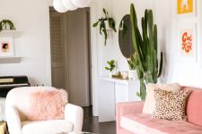 an elegant modern feminine living room with a pink sofa and a pouf, pink pillows, pretty artworks and a glass coffee table and potted cacti