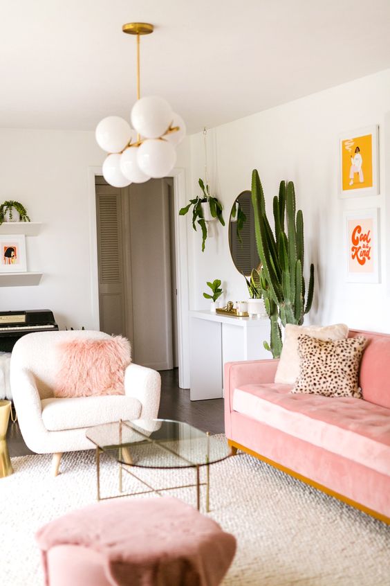 an elegant modern feminine living room with a pink sofa and a pouf, pink pillows, pretty artworks and a glass coffee table and potted cacti