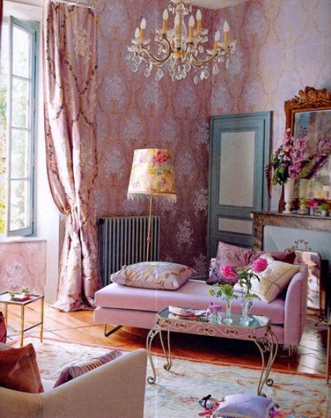 an exquisite feminine living room with beautiful pink wallpaper, a pink daybed, a chic chandelier, pink printed curtains and a faux fireplace