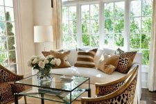 an exquisite living room done in neutrals, with a creamy sofa with printed pillows, leopard print chairs, layered rugs and a glass table