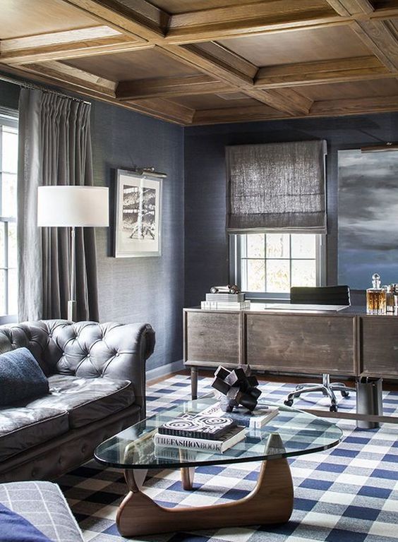 elegant grey and blue home office with a wooden desk, fabric curtains and shades, a leather sofa and a plaid rug