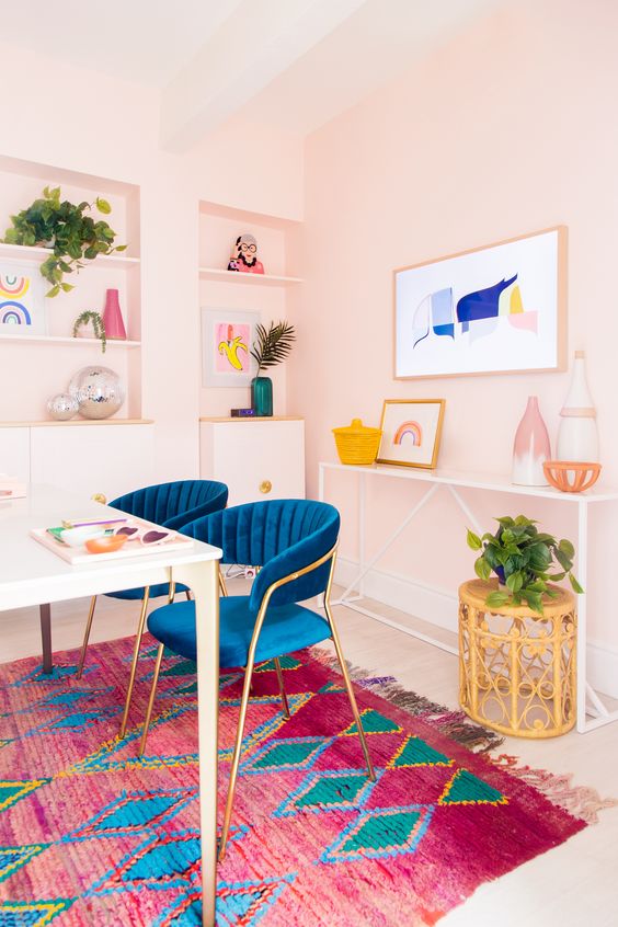 pink walls, a bright blue chairs, bright artworks and a bold rug make the space feel fun and spring or summer