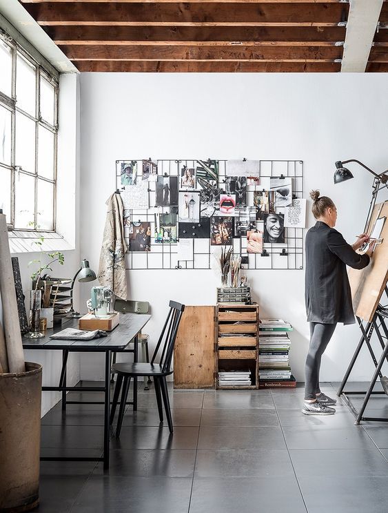 a Scandinavian artist studio with a black table and chair, a storage unit, a black grid as an inspirational board, an easel and black lamps