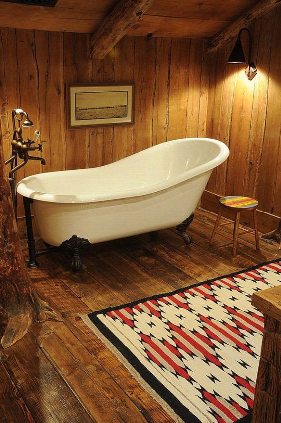 a barn bathroom fully decorated with wood, with a clawfoot tub, a bright rug and vintage fixtures and appliances