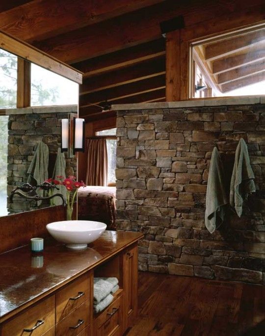 a barn bathroom with a stone wall, stained wood everywhere and a large mirror plus a bowl sink