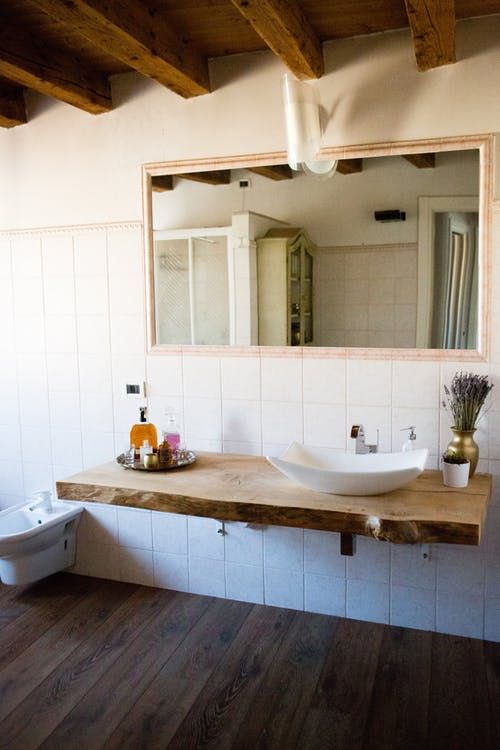 a barn bathroom with a wooden ceiling with beams, white tiles, a wall-mounted wooden vanity and a large mirror