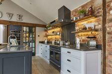 a barn kitchen with a brick accent wall, white cabinets and a stone blue kitchen island, wooden beams and stainless steel appliances