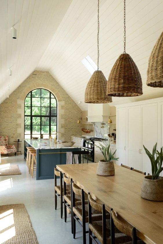 a barn kitchen with a stone accent wall, an arched window, white shaker style cabinets, a stone blue kitchen island and woven pendant lamps