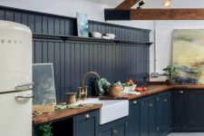 a barn kitchen with wooden beams, graphite grey cabinets, butcherblock countertops, pendant bulbs and brass fixtures