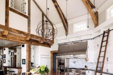 a barn kitchen with wooden beams, white shaker style cabinets, a grey planked kitchen island that doubles as a table